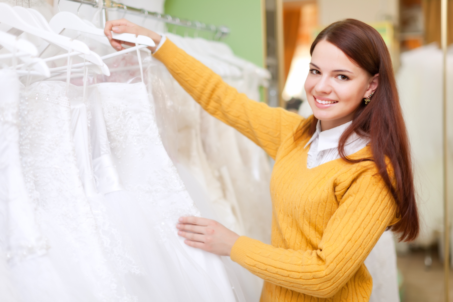 A bride-to-be examining a wedding gown on a rack in a beautifully decorated wedding clothing store.